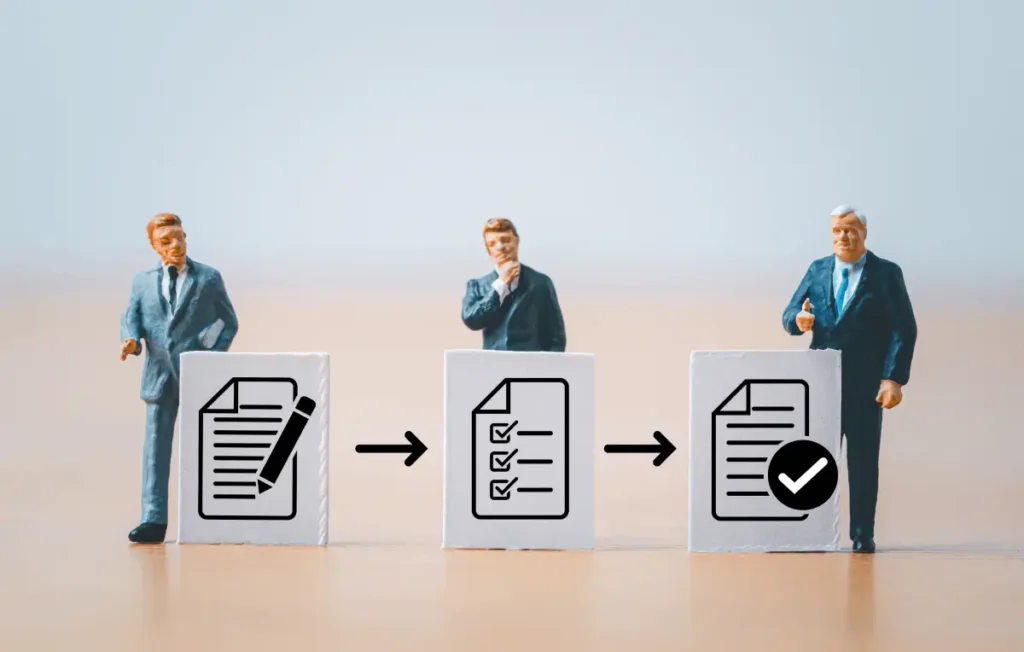 Miniature figurines of businessmen stand next to blocks showing icons of documents with arrows between them, symbolizing a step-by-step application or approval process.