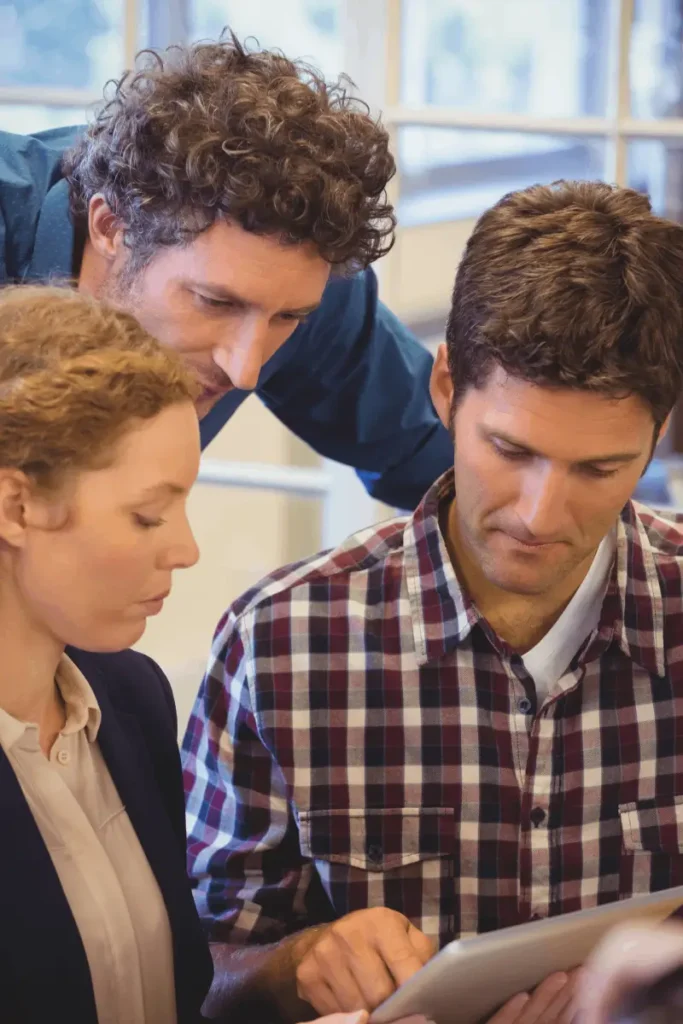 Three colleagues closely reviewing information on a tablet during a discussion.