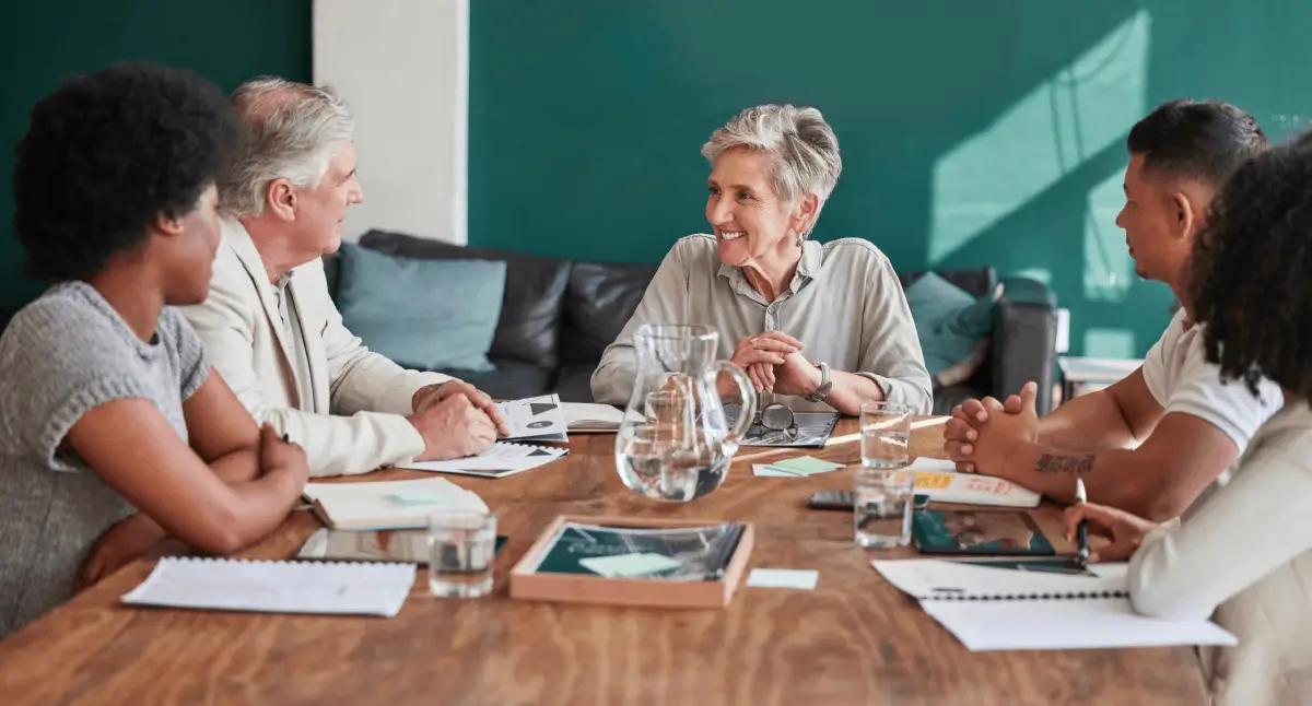 A group of five people sit around a wooden table, engaged in a positive and collaborative discussion.