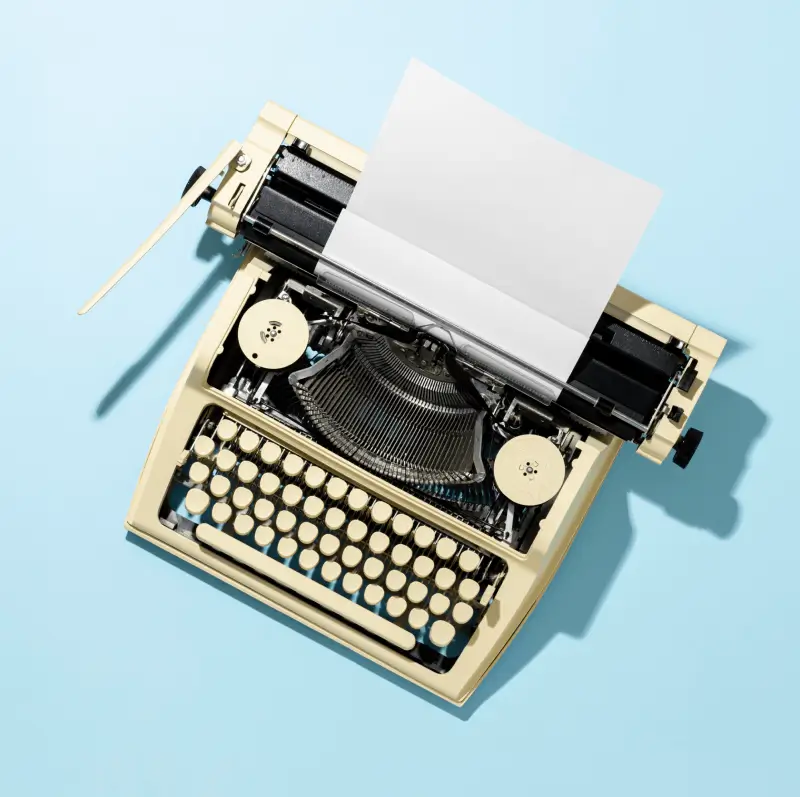 A vintage typewriter with a blank sheet of paper inserted, placed on a light blue background.