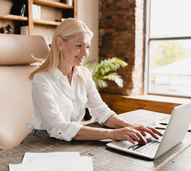 Side view portrait of a confident smiling caucasian businesswoman boss working in office, typing on laptop computer, searching information web, social media, watching webinars online